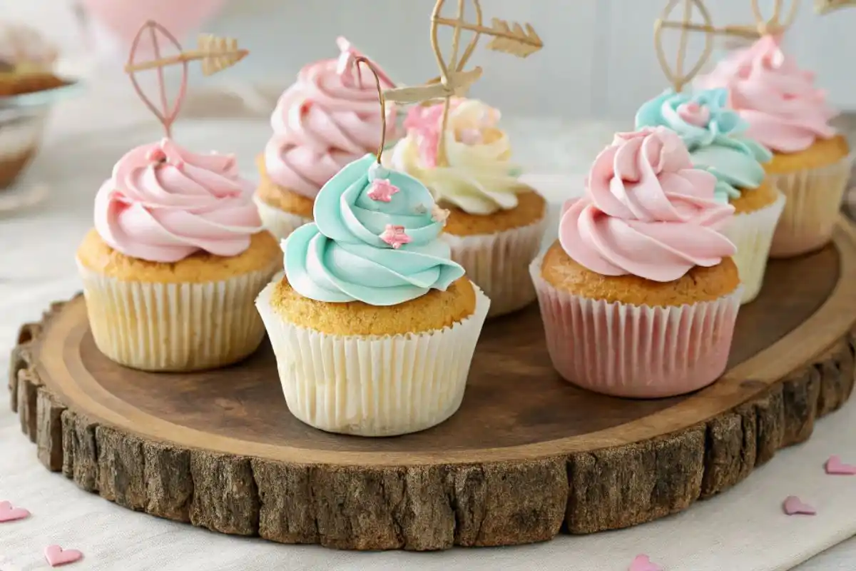 A tray of bow arrow cupcakes with pastel frosting and edible bow and arrow toppers, set against a festive backdrop